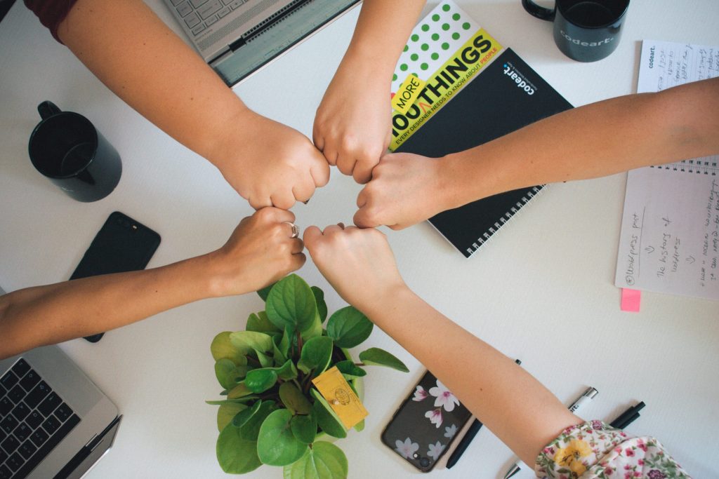 Five hands doing a group fist bump over an office desk.