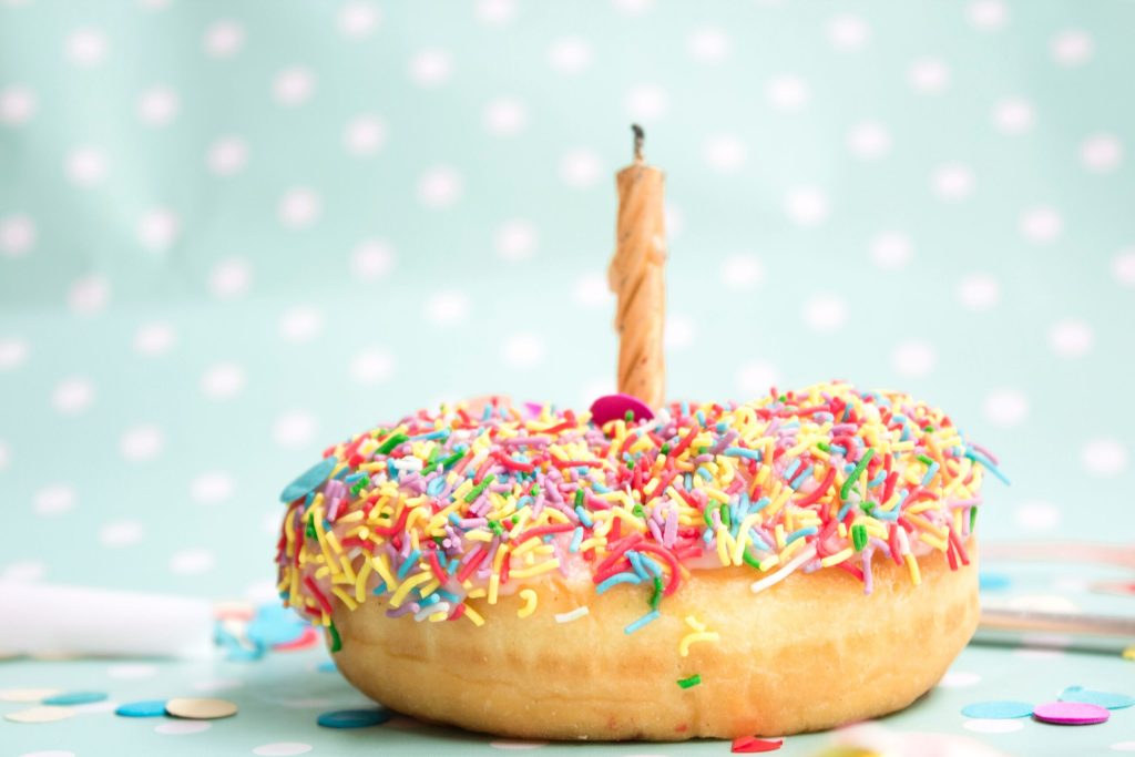 A donut with coloured sprinkles and a birthday candle in the middle.