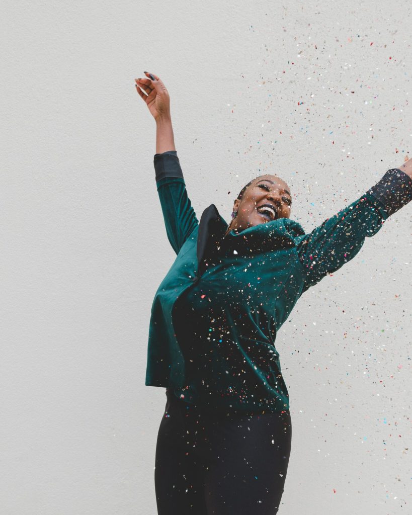 A person throwing their hands up in joy in a cloud of confetti